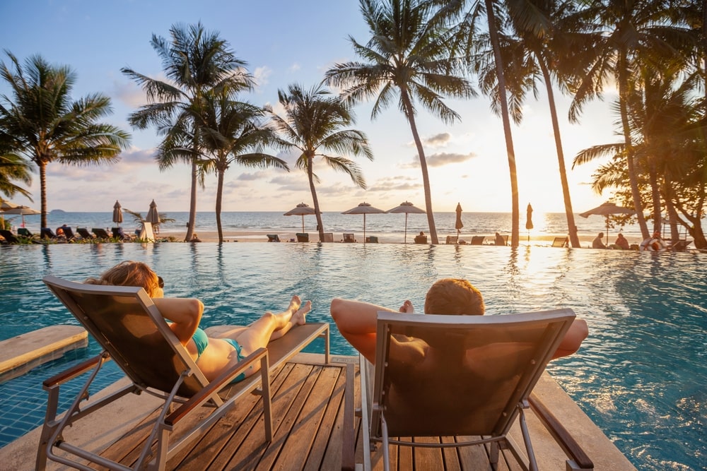 A Couple Lounging In Chairs Next To A Pool