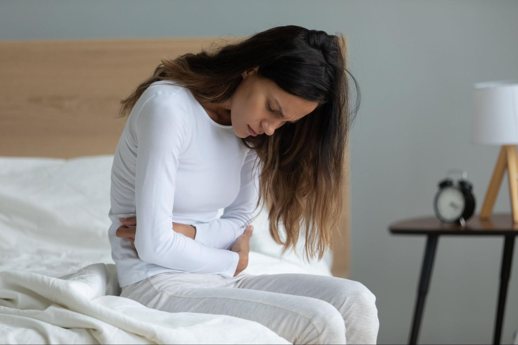 Woman sitting on bed and holding her stomach